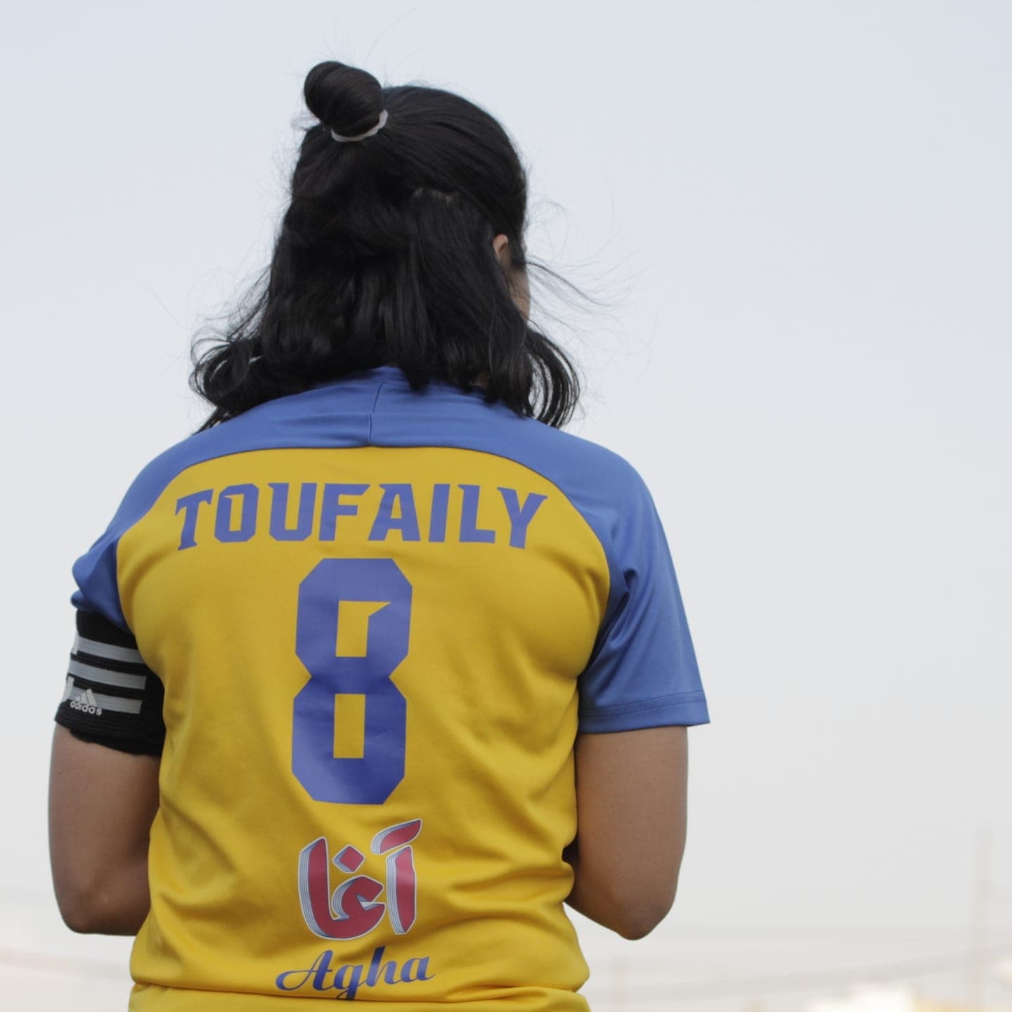 Assile Toufaily seen from behind in a yellow and blue club shirt with her name and the number 8